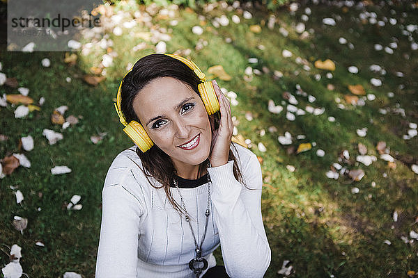 Glückliche schöne Frau hört Musik  während sie im Park sitzt