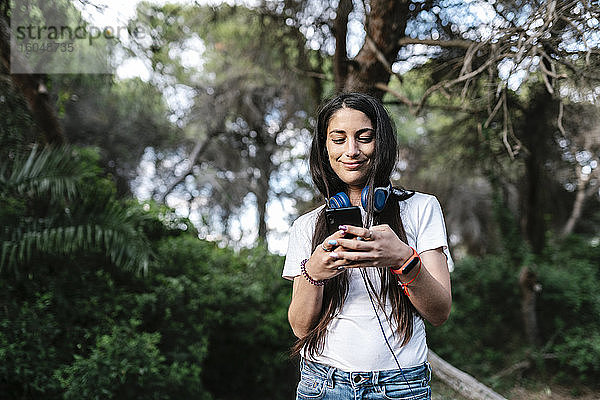 Frau mit Headset und Smartphone im Wald