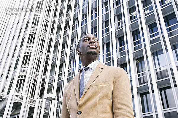 Junger Geschäftsmann vor einem modernen Bürogebäude in der Stadt  der zur Seite schaut