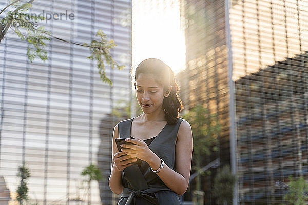Geschäftsfrau  die ein Smartphone benutzt  während sie vor modernen Gebäuden in der Stadt steht