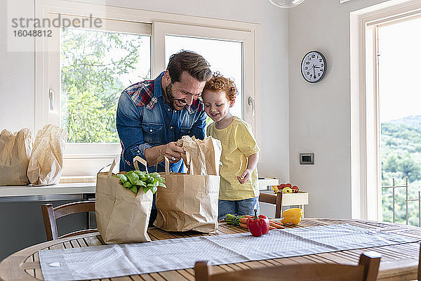 Lächelnder Mann zeigt seinem Sohn in der Küche zu Hause Lebensmittel