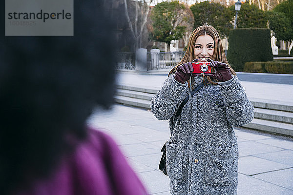 Fröhliche Frau  die ihre Freundin fotografiert  während sie auf der Straße in der Stadt steht
