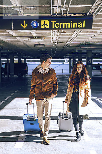 Ein Geschäftspaar zieht sein Gepäck  während es unter dem Terminalschild am Flughafen läuft