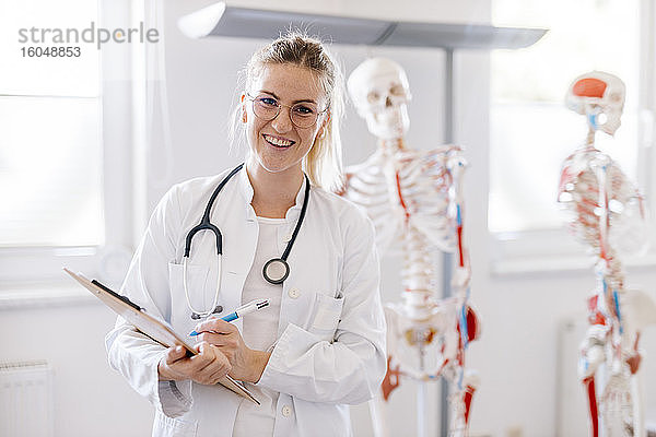 Porträt einer lächelnden Ärztin mit anatomischem Skelett im Hintergrund