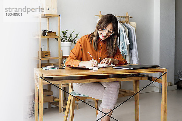 Weibliche Modedesignerin  die zu Hause am Schreibtisch sitzt und Notizen macht