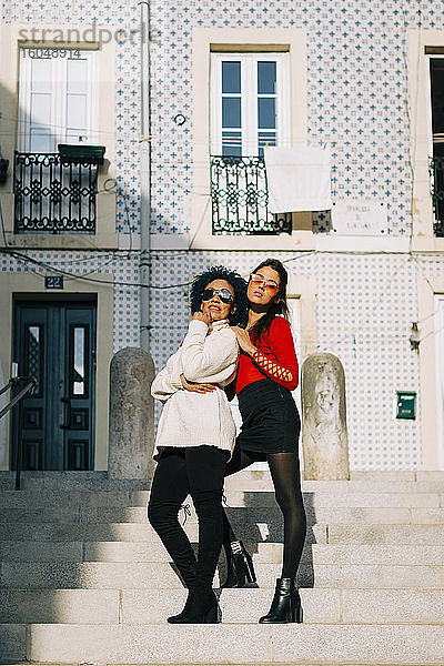 Freundinnen mit Sonnenbrillen stehen auf den Stufen eines Gebäudes in der Stadt
