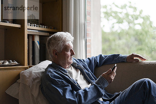 Älterer Mann benutzt sein Smartphone  während er sich zu Hause auf dem Sofa entspannt