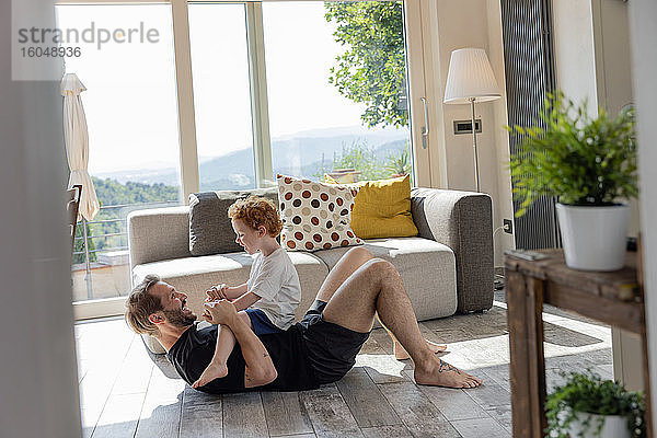Glücklicher Mann  der mit seinem süßen Sohn spielt  während er im Wohnzimmer auf dem Sofa liegt
