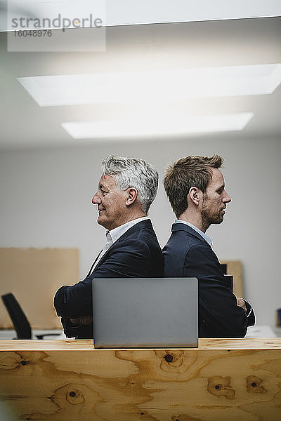 Zwei selbstbewusste Geschäftsleute sitzen im Büro mit Laptop  Rücken an Rücken