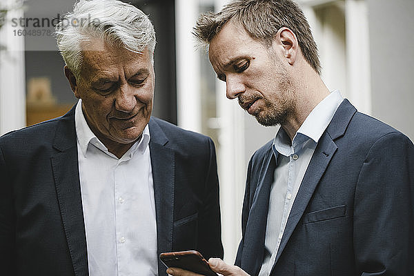 Zwei Geschäftsleute stehen im Hinterhof und benutzen ein Smartphone