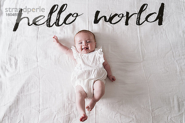 Happy cute baby girl lying on blanket under Hello World text at home