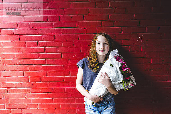 Mädchen hält Blumenstrauß und steht vor einer roten Wand in der Stadt
