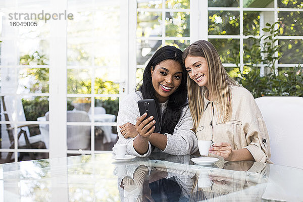 Glückliche multiethnische Freundinnen machen ein Selfie mit ihrem Smartphone am Tisch in einem Café