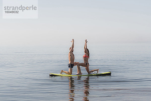 Paar übt gemeinsam Yoga auf dem Paddelbrett über dem Meer