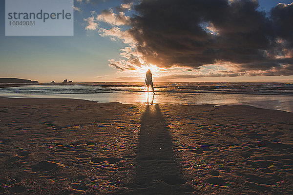 Silhouette junge Frau steht am Strand gegen den Himmel bei Sonnenuntergang