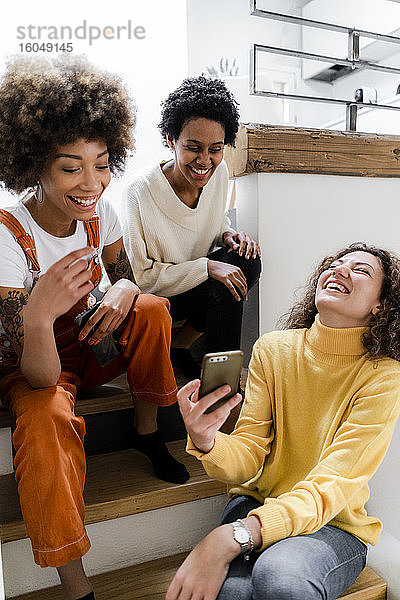 Drei lachende junge Frauen haben Spaß mit dem Smartphone zu Hause