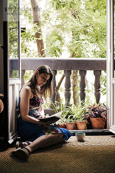 Frau liest ein Buch  während sie zu Hause auf dem Balkon sitzt