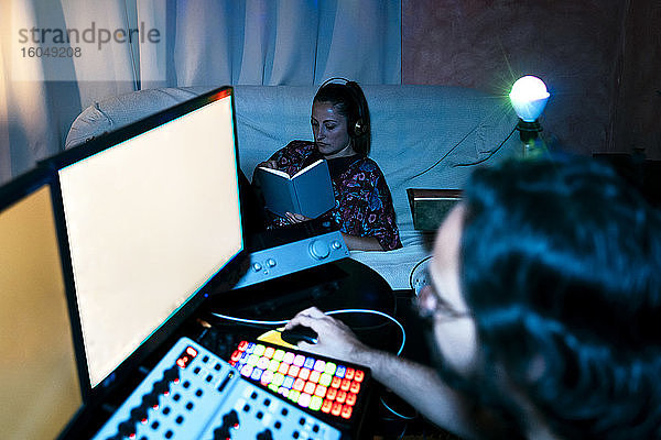 Mann am Computer  während Frau im Aufnahmestudio zu Hause ein Buch liest