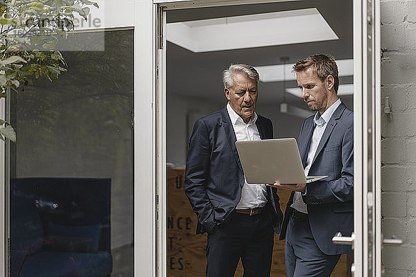 Zwei selbstbewusste Geschäftsleute  die einen Laptop benutzen und in der Bürotür stehen