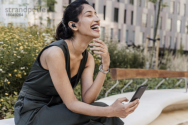 Fröhliche Geschäftsfrau mit Videogespräch über Smartphone in der Stadt sitzend