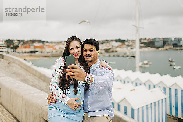 Ein schwangeres Paar macht ein Selfie mit seinem Smartphone am Hafen  Cascais  Portugal
