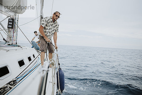 Matrosen entfernen Stoßstangen auf einem Segelboot im Meer gegen den Himmel