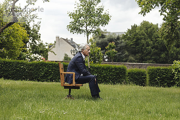 Älterer Geschäftsmann sitzt auf einem Stuhl in einem ländlichen Garten