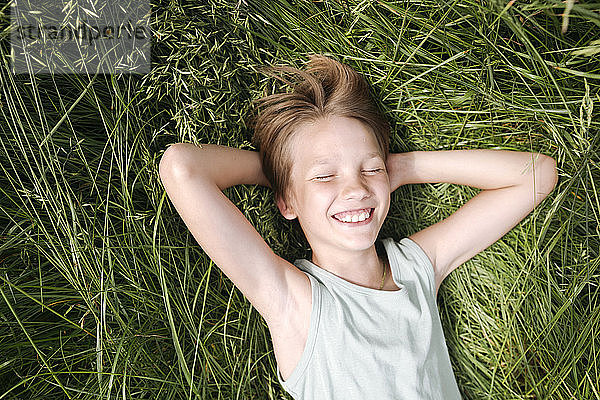 Porträt eines glücklichen Jungen mit geschlossenen Augen  der im Sommer auf einer Wiese liegt
