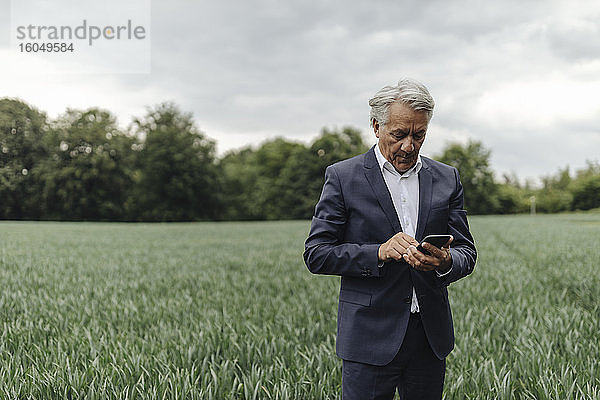 Ein älterer Geschäftsmann benutzt sein Smartphone auf einem Feld auf dem Lande