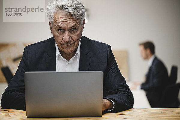 Älterer Geschäftsmann arbeitet am Laptop  sitzt mit Kollegen im Büro