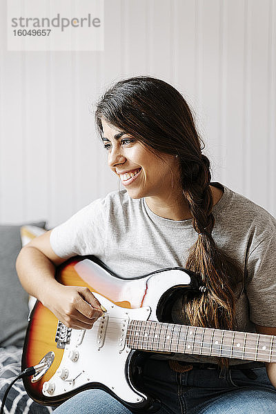 Glückliche Frau spielt E-Gitarre  während sie zu Hause sitzt