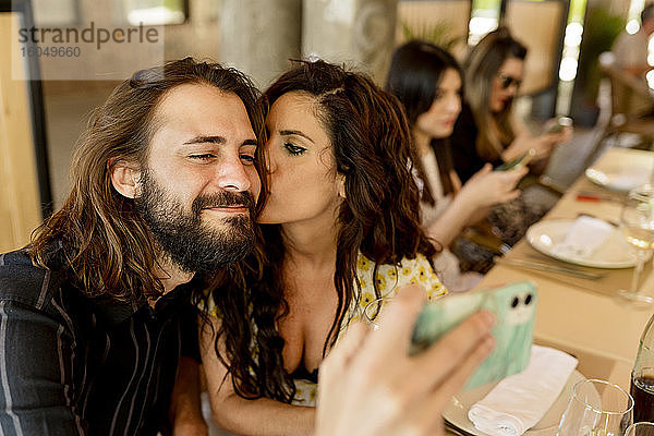 Mann macht Selfie  während Frau ihn im Restaurant küsst