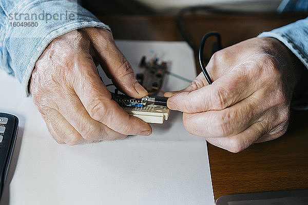 Ausgeschnittenes Bild eines älteren Mannes  der die USB-Platine eines Laptops zu Hause repariert
