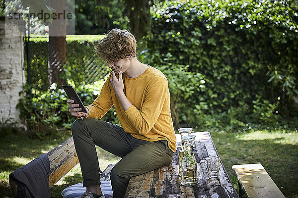 Junger Mann sitzt am Biertisch im Garten und benutzt ein digitales Tablet