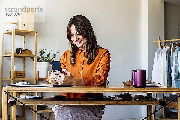 Modedesignerin  die zu Hause am Schreibtisch sitzt und ein Smartphone benutzt