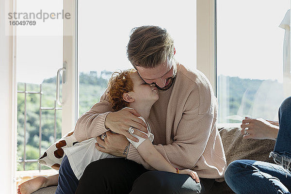 Mann umarmt süßen Vorschulsohn  während er bei einer Frau im Wohnzimmer sitzt