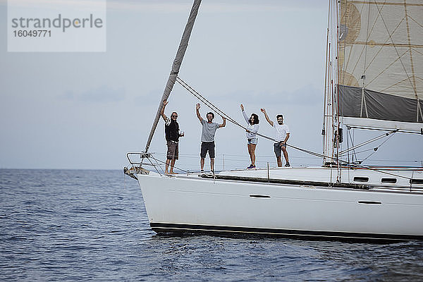 Glückliche Freunde winken  während sie auf einem Segelboot im Meer stehen