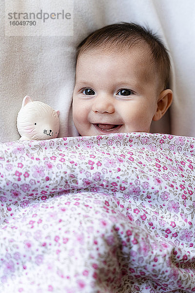 Porträt eines glücklichen kleinen Mädchens auf dem Bett liegend mit Beißring