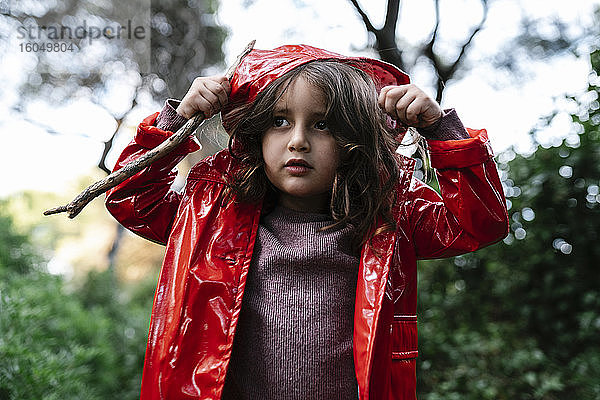 Mädchen mit roter Regenjacke und Kapuze im Wald