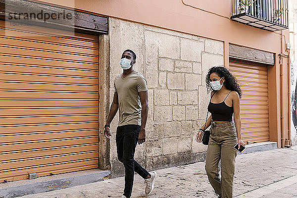 Mann und Frau tragen Masken  während sie durch die Stadt gehen