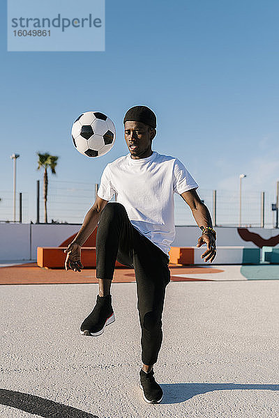 Junger Mann jongliert mit Fußball gegen den klaren Himmel im Hof