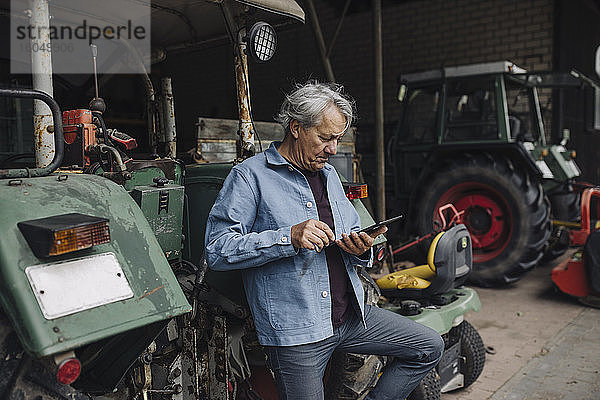 Älterer Mann mit Tablet auf einem Bauernhof mit Traktor in der Scheune