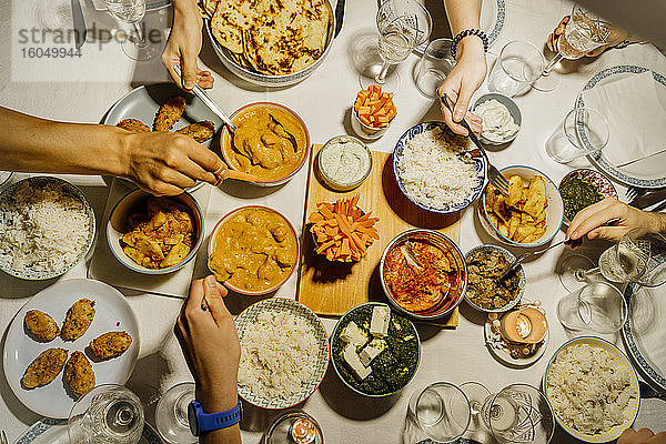 Hände von Menschen  die gemeinsam an einem mit indischen Speisen gedeckten Tisch essen