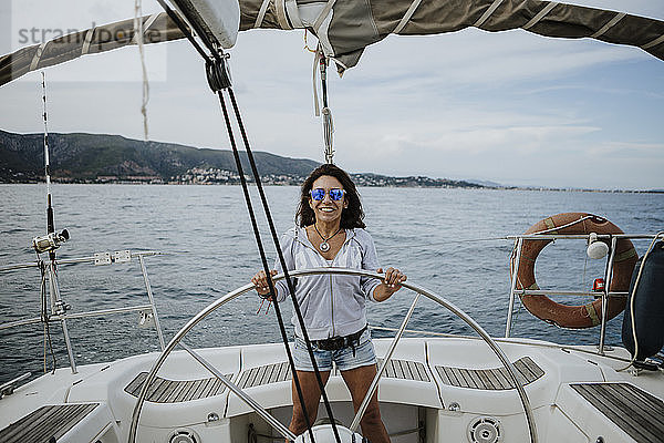 Glückliche Seglerin mit Sonnenbrille  die ein Segelboot auf dem Meer fährt