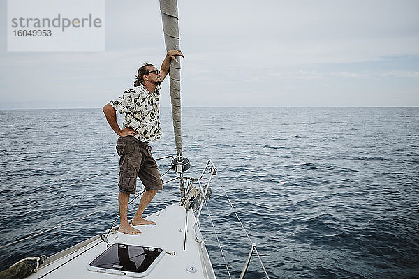 Männlicher Seemann steht auf dem Bug eines Segelbootes im Meer gegen den Himmel