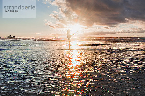 Silhouette Frau tanzend im Meer stehend gegen den Himmel bei Sonnenuntergang