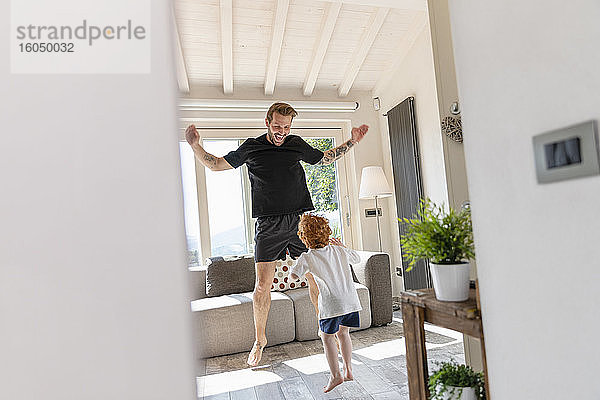 Fröhlicher Vater und Sohn springen beim Spielen im heimischen Wohnzimmer