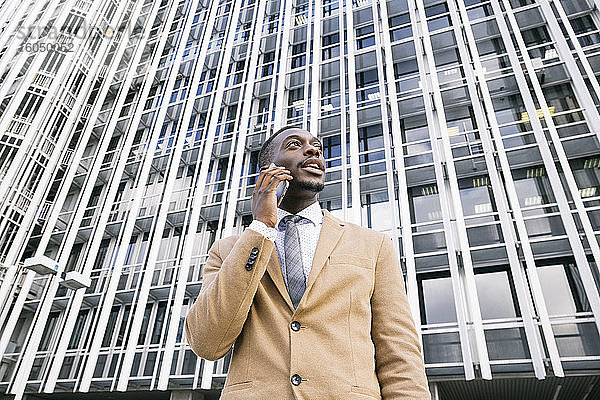Junger Geschäftsmann vor einem modernen Bürogebäude in der Stadt beim Telefonieren
