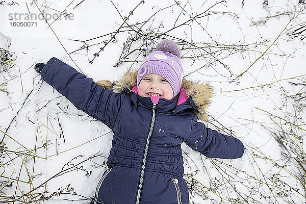 Glückliches Mädchen liegt mit ausgestreckten Armen im Schnee