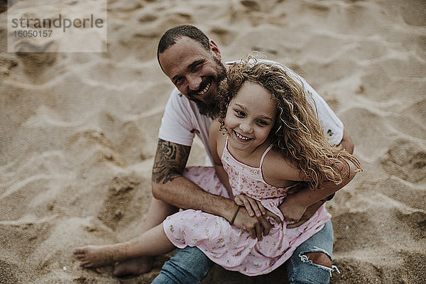 Tochter sitzt auf dem Schoß des Vaters und spielt am Strand